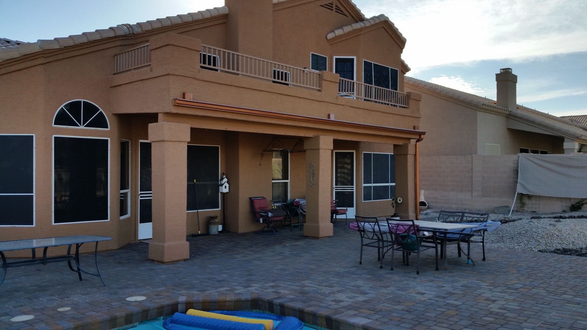 Two-story tan stucco house with patio furniture and a trampoline in the backyard