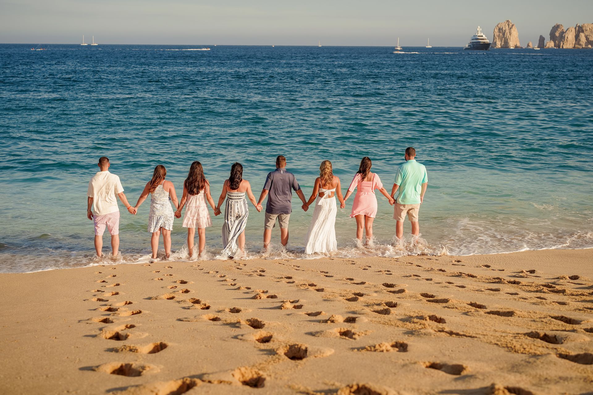 A group of people standing on a beach, holding hands, facing the ocean.
