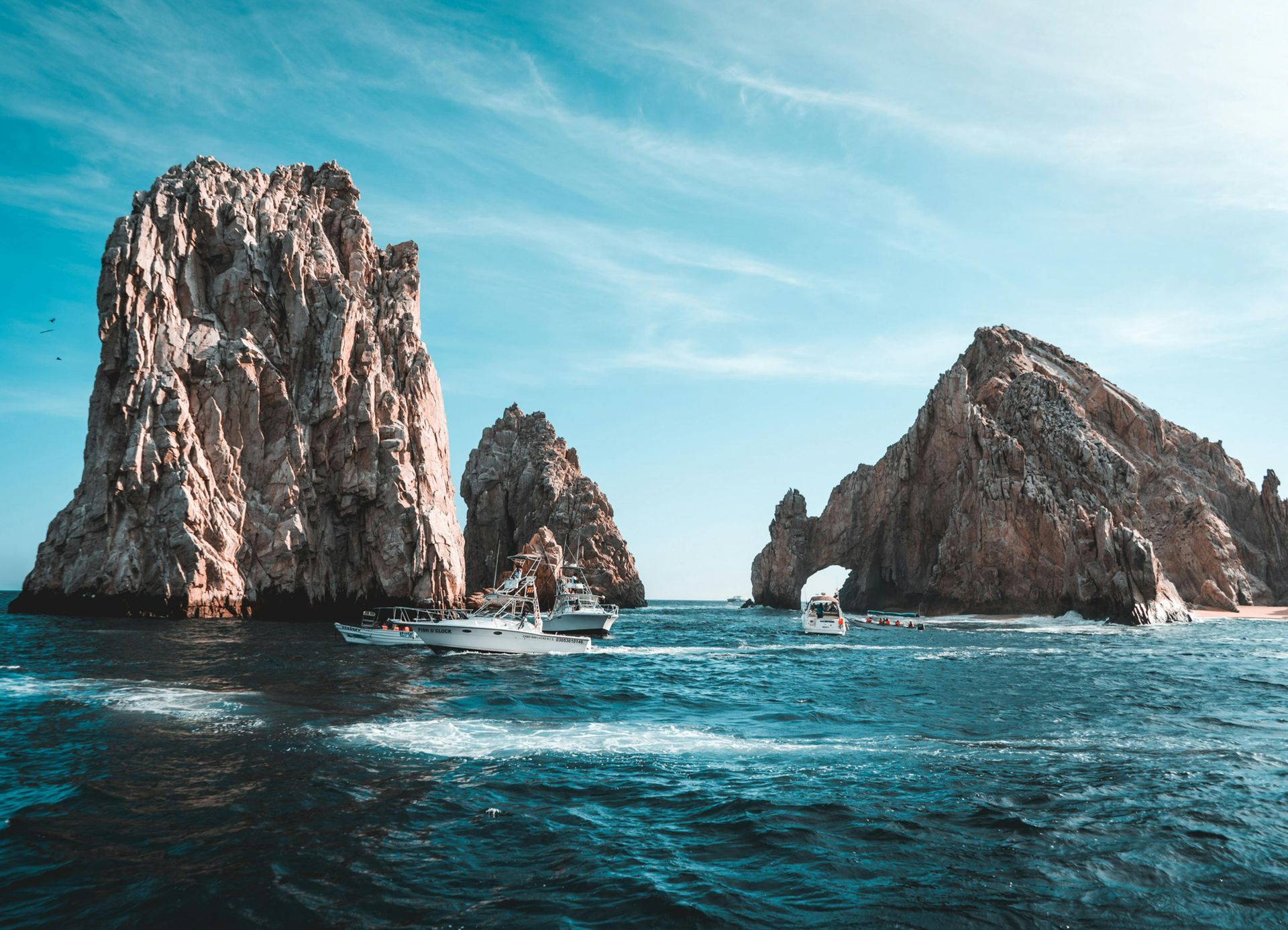 Rocky sea cliffs with boats in clear blue water under a sunny sky.