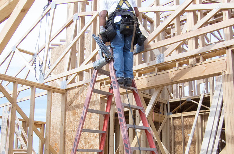 A man is standing on a ladder in front of a building under construction