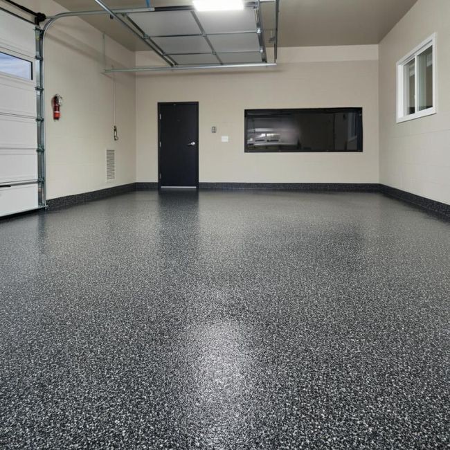 Empty garage with speckled epoxy floor, black door, and interior windows on beige walls.