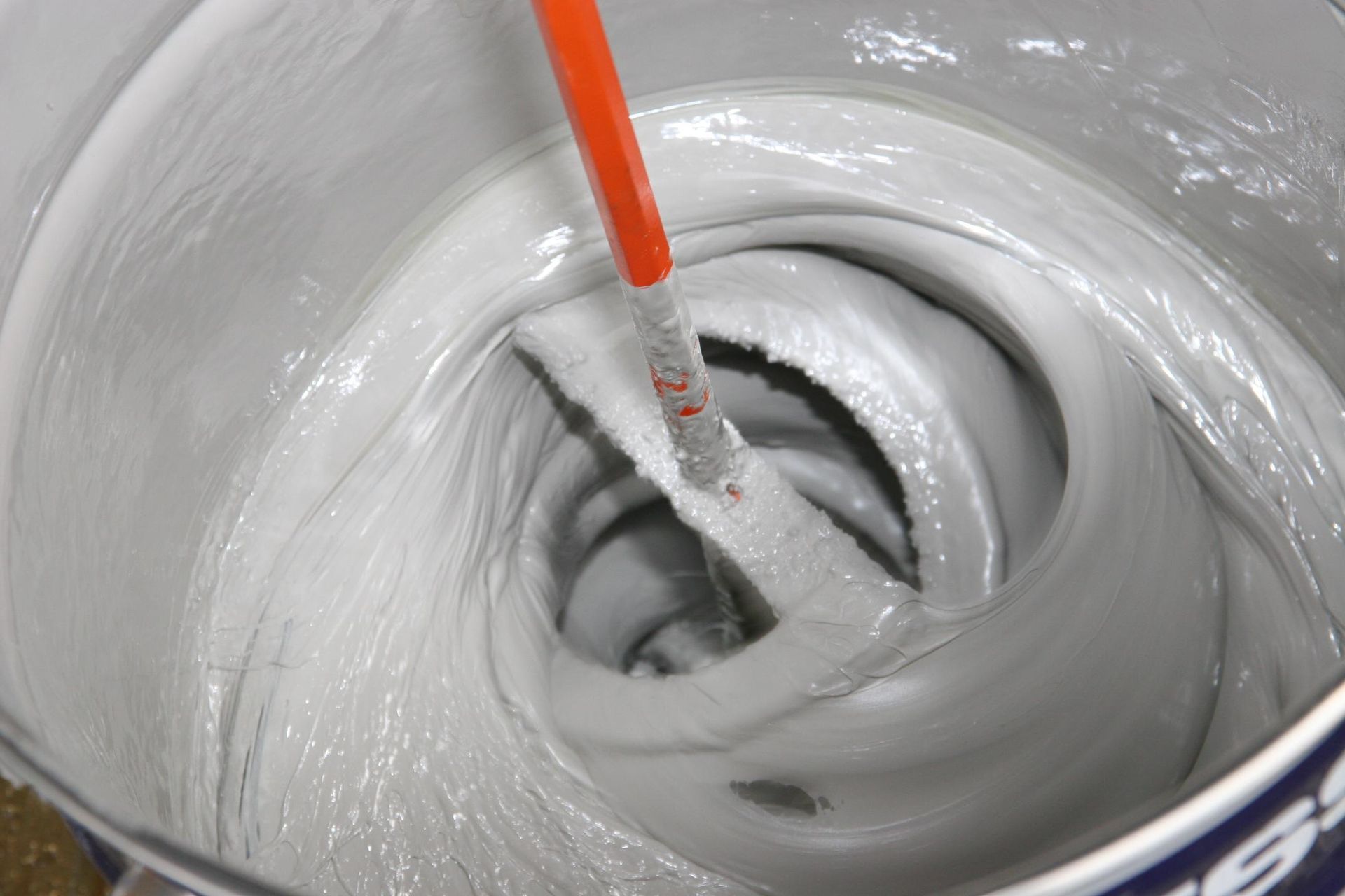 Paint stirrer mixing thick white paint in a can