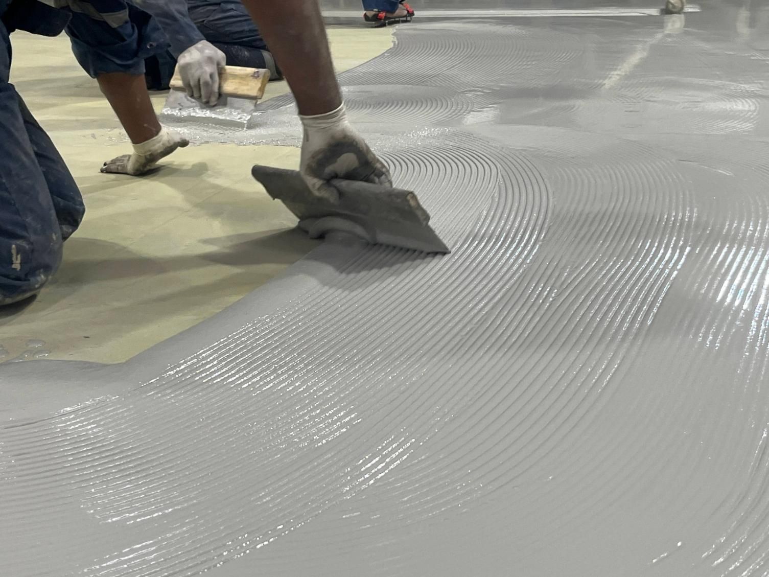 Workers smoothing gray floor coating with trowels inside an indoor construction area