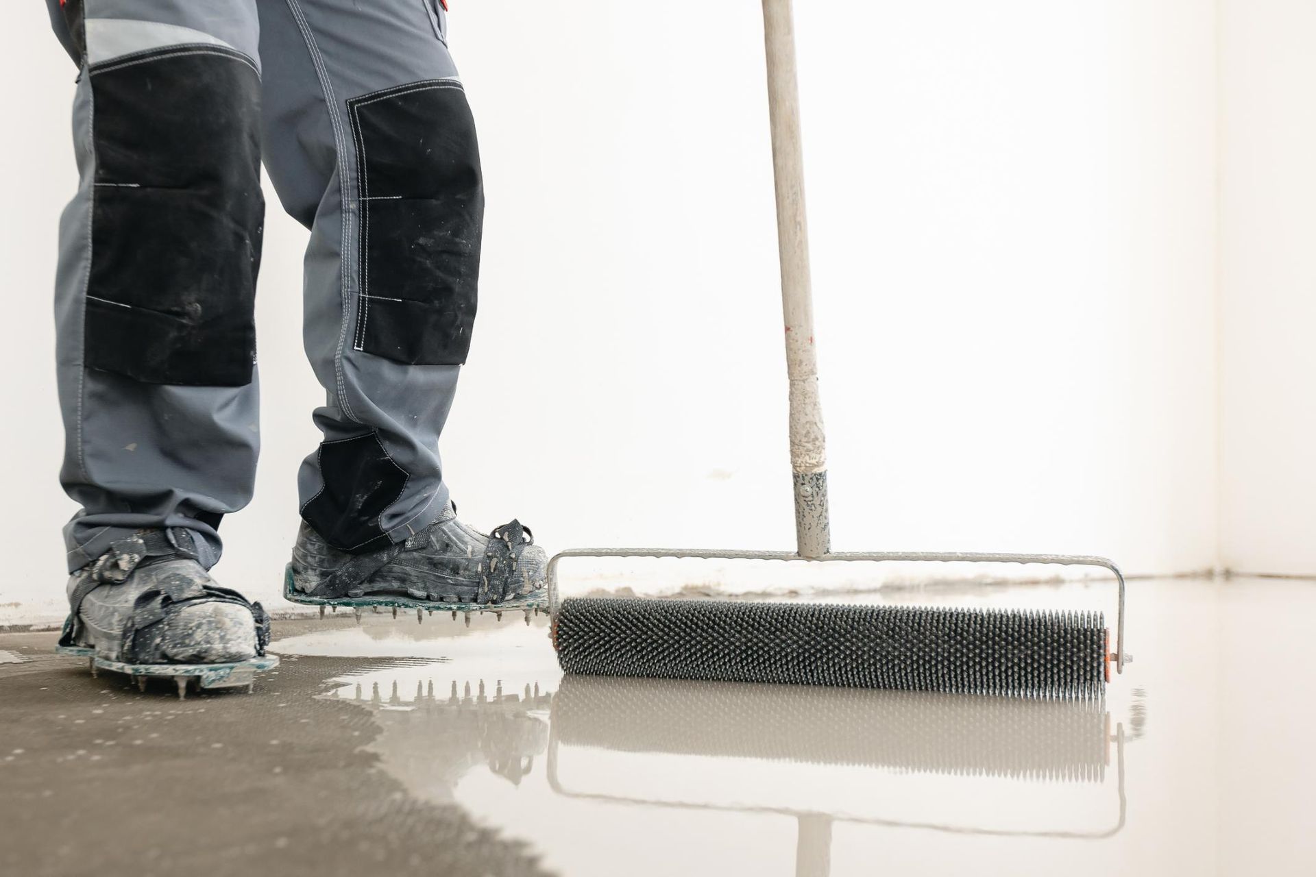 Worker spreading wet concrete with a roller on a floor indoors