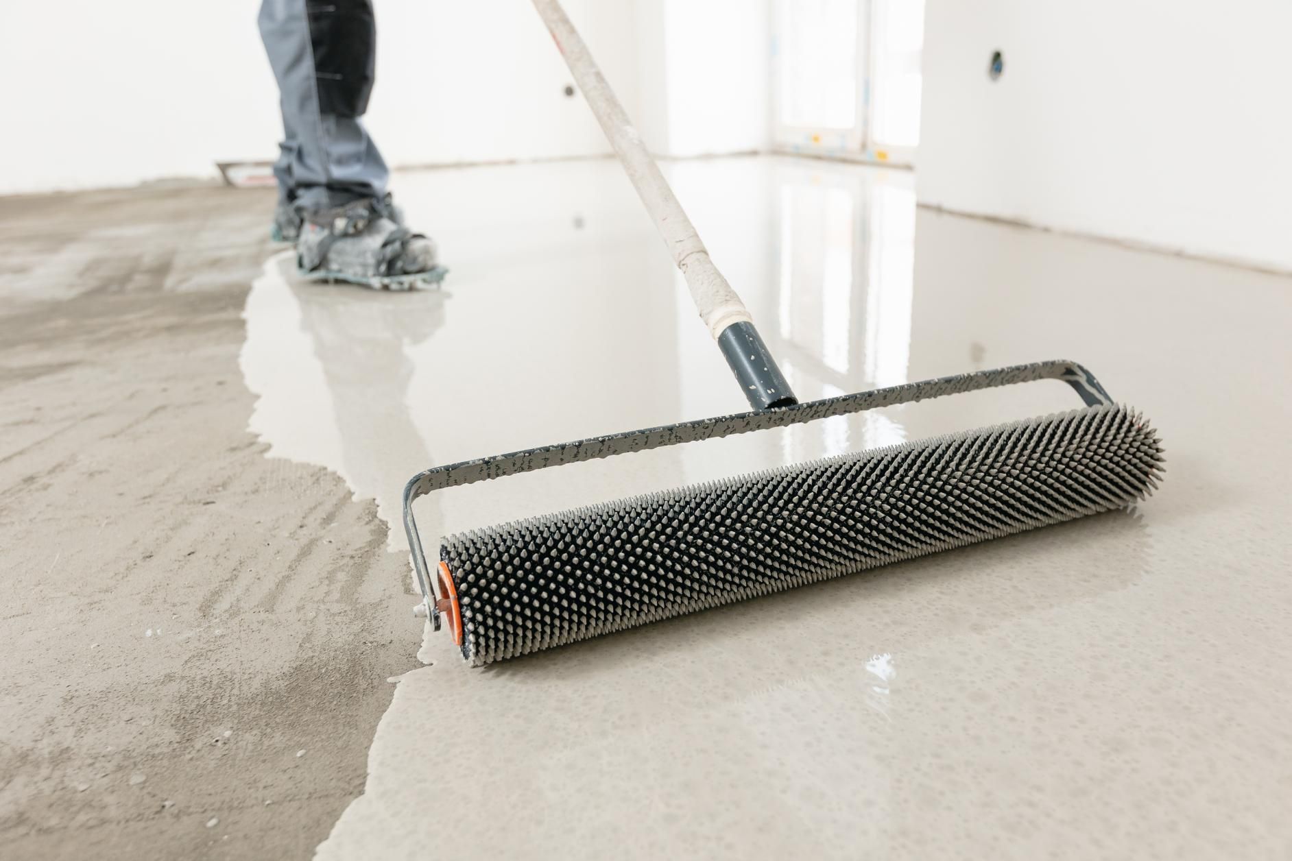 Person spreading gray concrete with a roller on a wet floor indoors