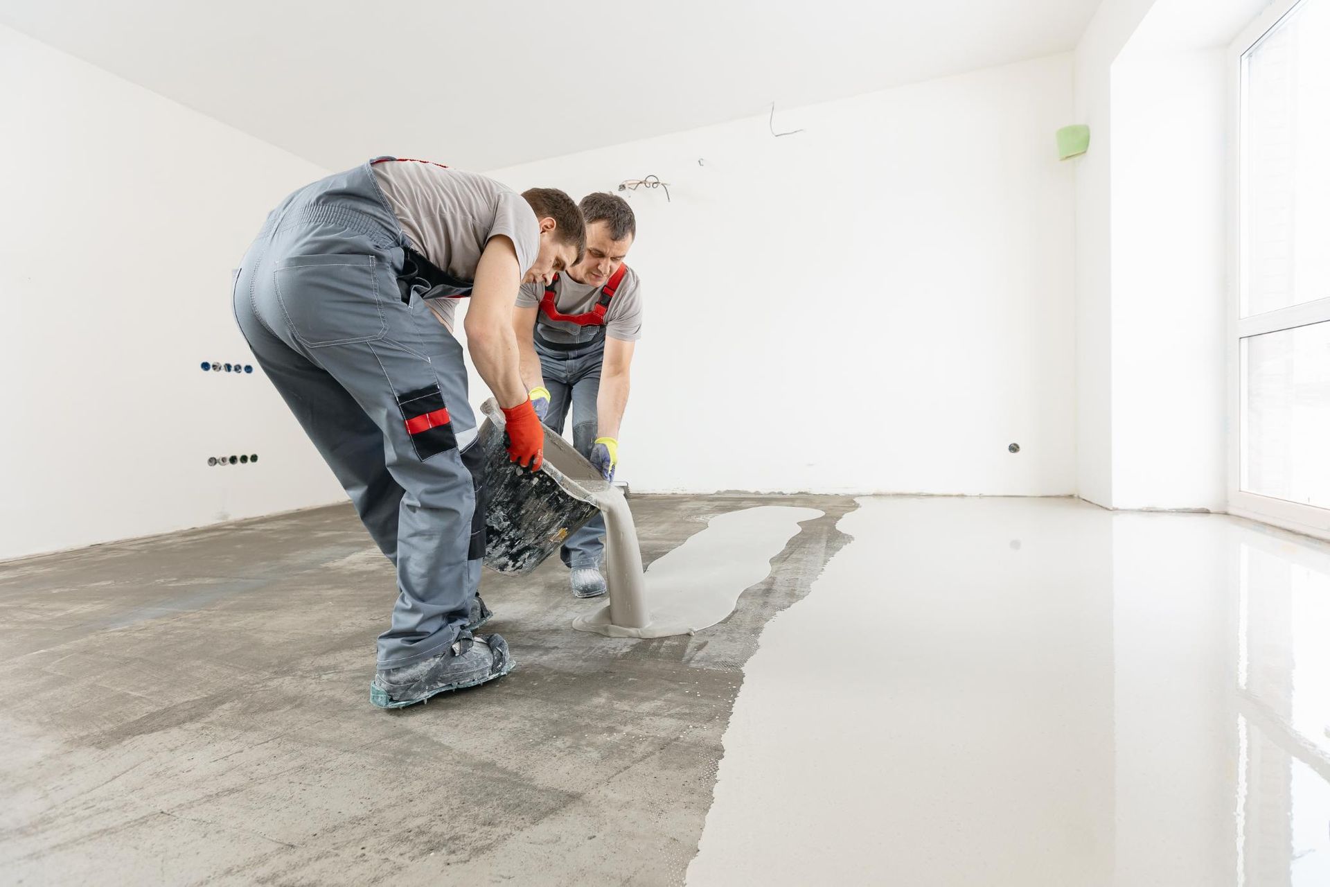 Workers smoothing wet concrete floor in a bright empty room