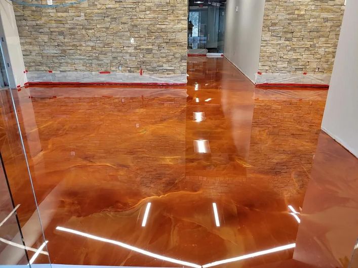 Shiny orange epoxy floor in a hallway with stone walls and white door frames
