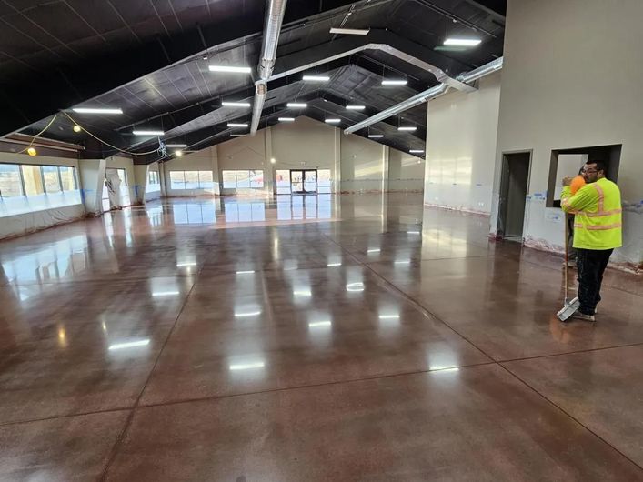 Spacious empty hall with polished wooden floor and a person in a yellow jacket standing by the wall