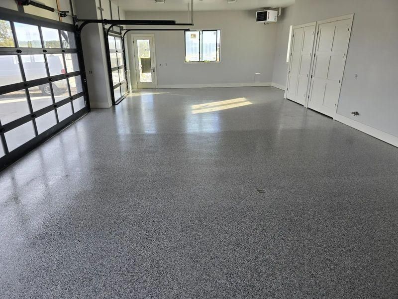 Empty gray garage with polished floor, large glass door, white walls, and a small window.