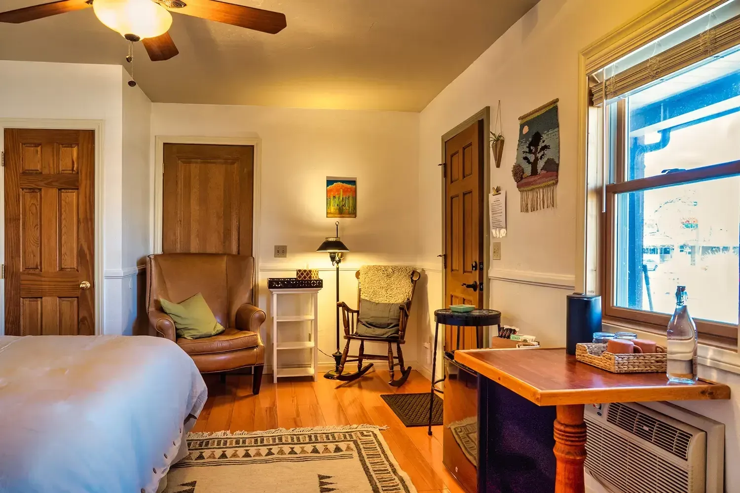 A bedroom with a bed , chair , table and ceiling fan.