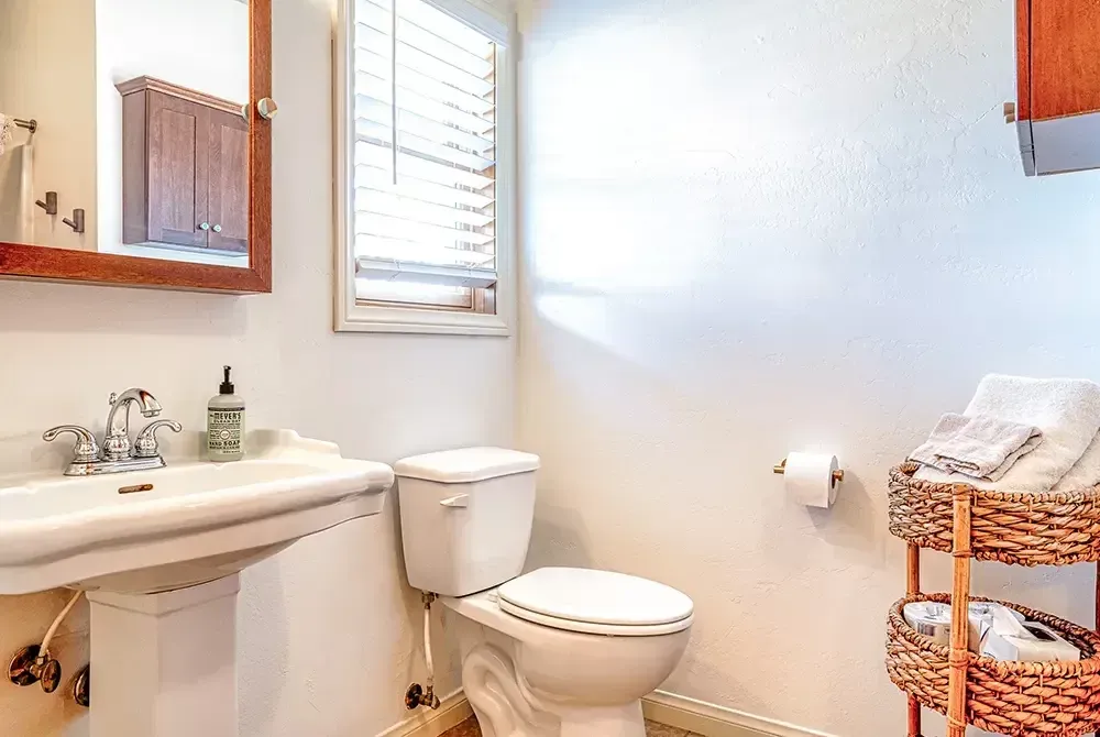 A bathroom with a toilet , sink , mirror and window.