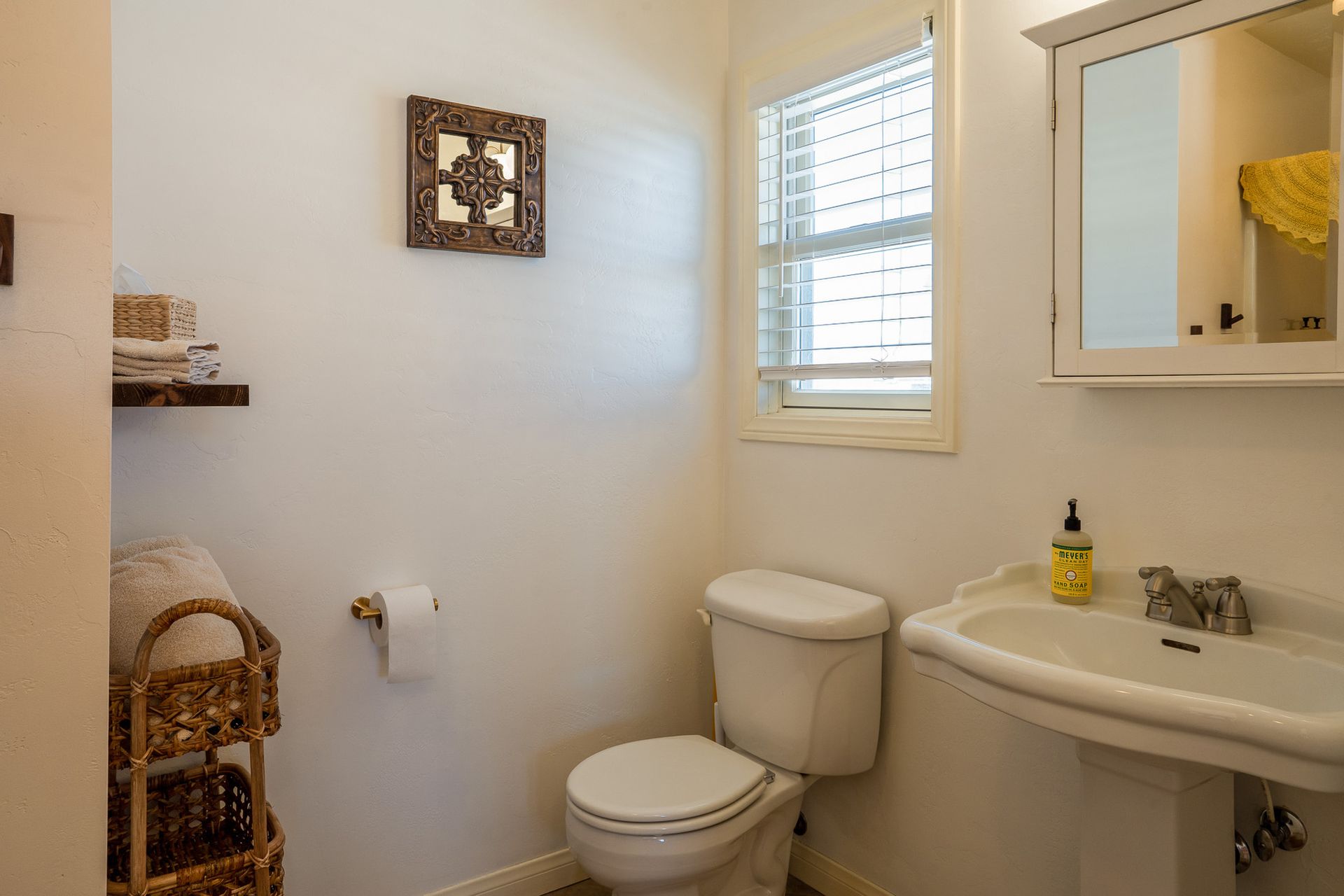A bathroom with a toilet , sink , mirror and window.