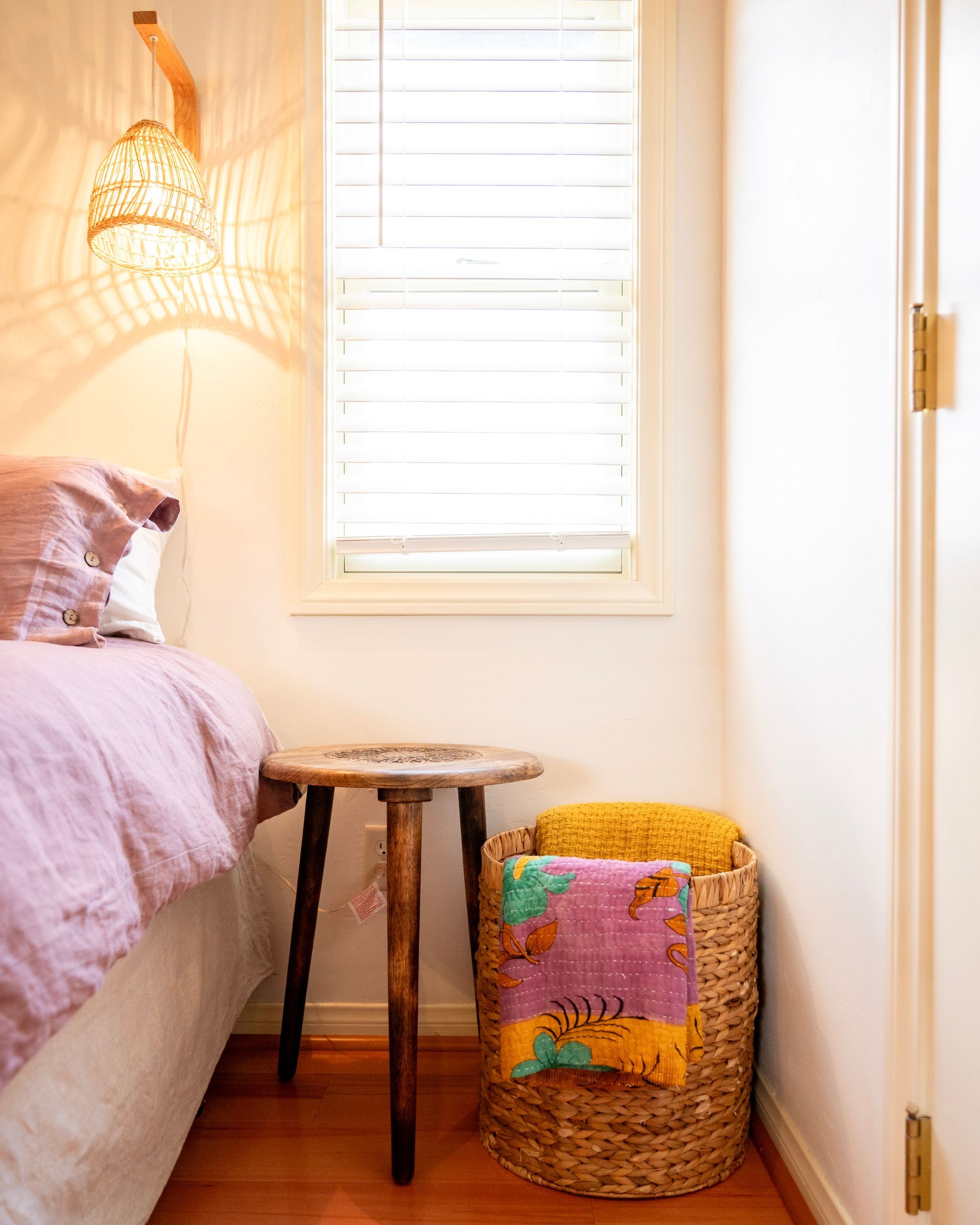 A bedroom with a bed , nightstand , basket and window.