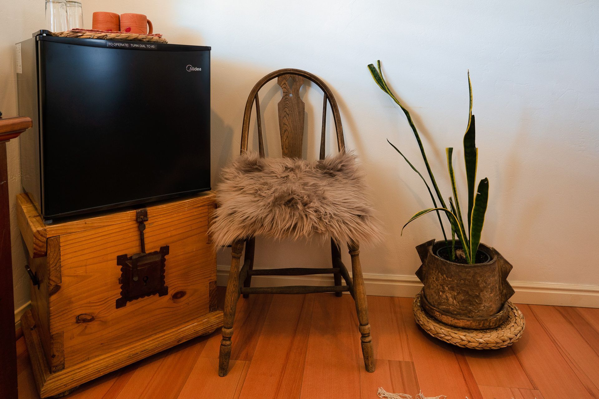 A chair is sitting next to a small refrigerator and a potted plant.