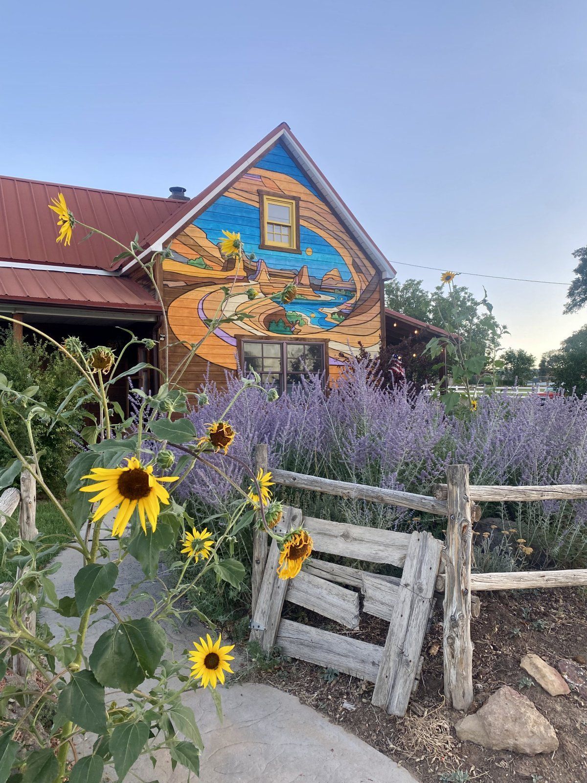 A house with a mural on the side of it and flowers in front of it.