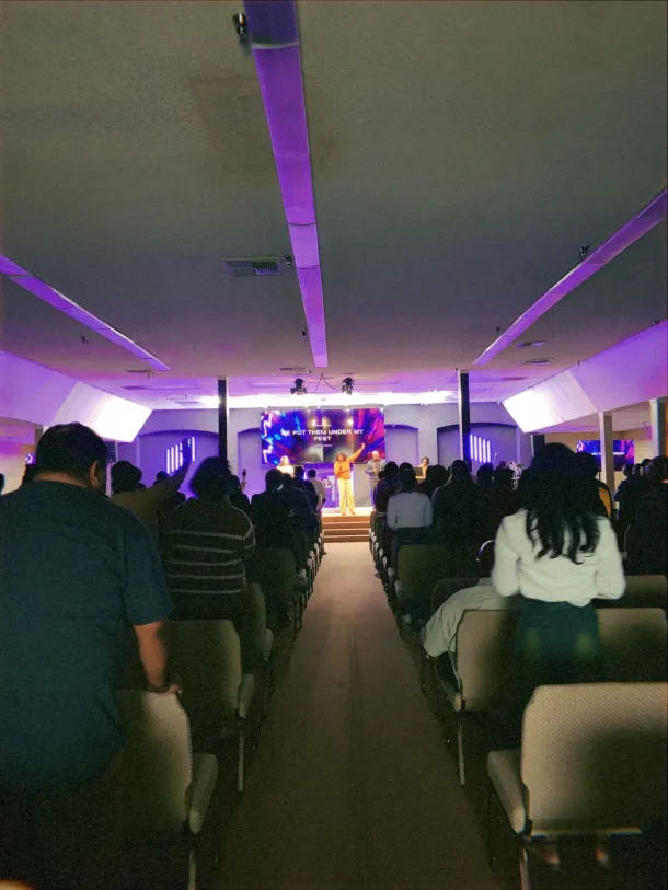 People in a church auditorium; a person at a podium lit with purple lights.