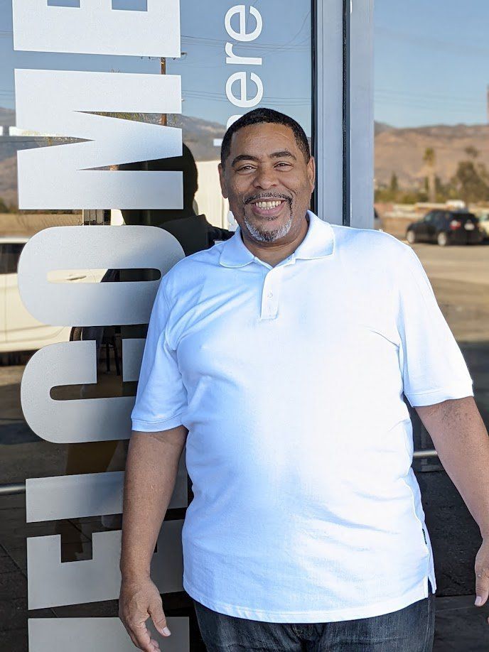 Man in white polo shirt smiles in front of a building with the word 
