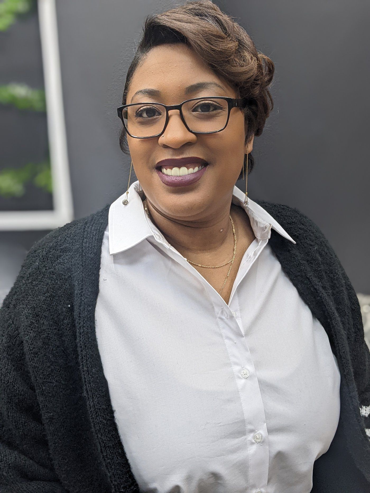 Woman wearing glasses, smiling, dressed in a white shirt and black cardigan.