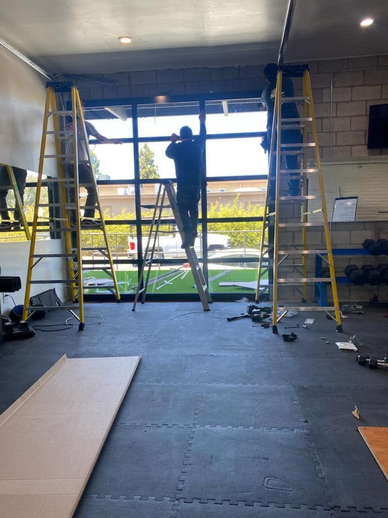 Person on a ladder installing a large window in an unfinished indoor room