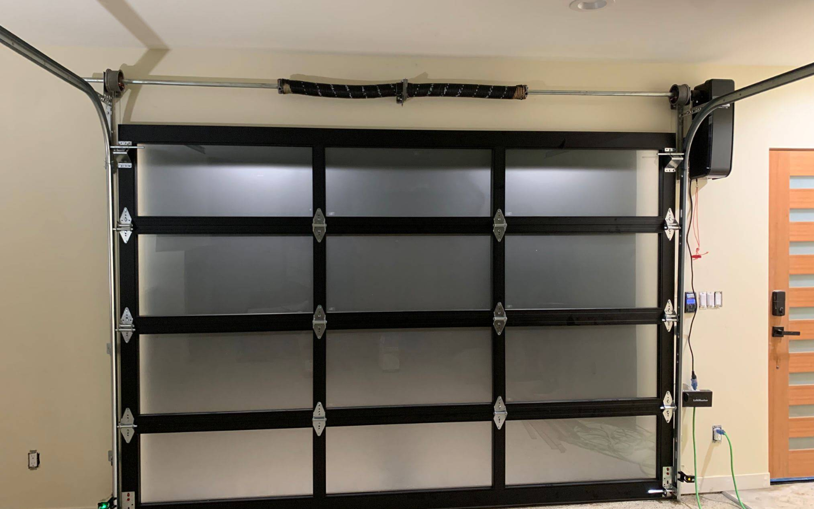 Garage with a black multi-panel overhead door and empty shelving units on either side