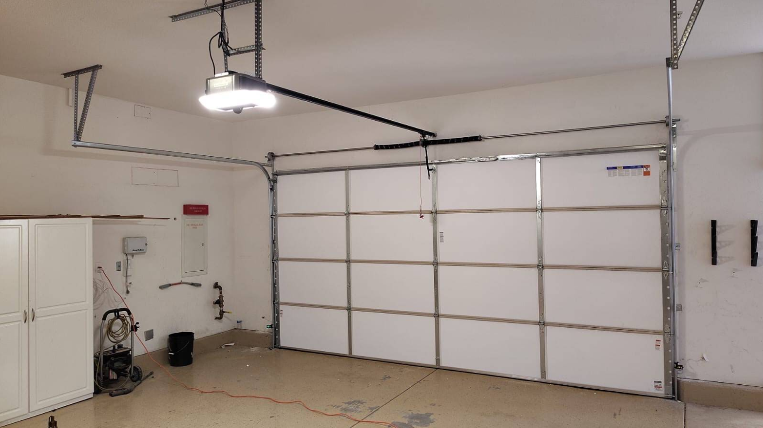 Empty garage interior with white sectional door and overhead opener system