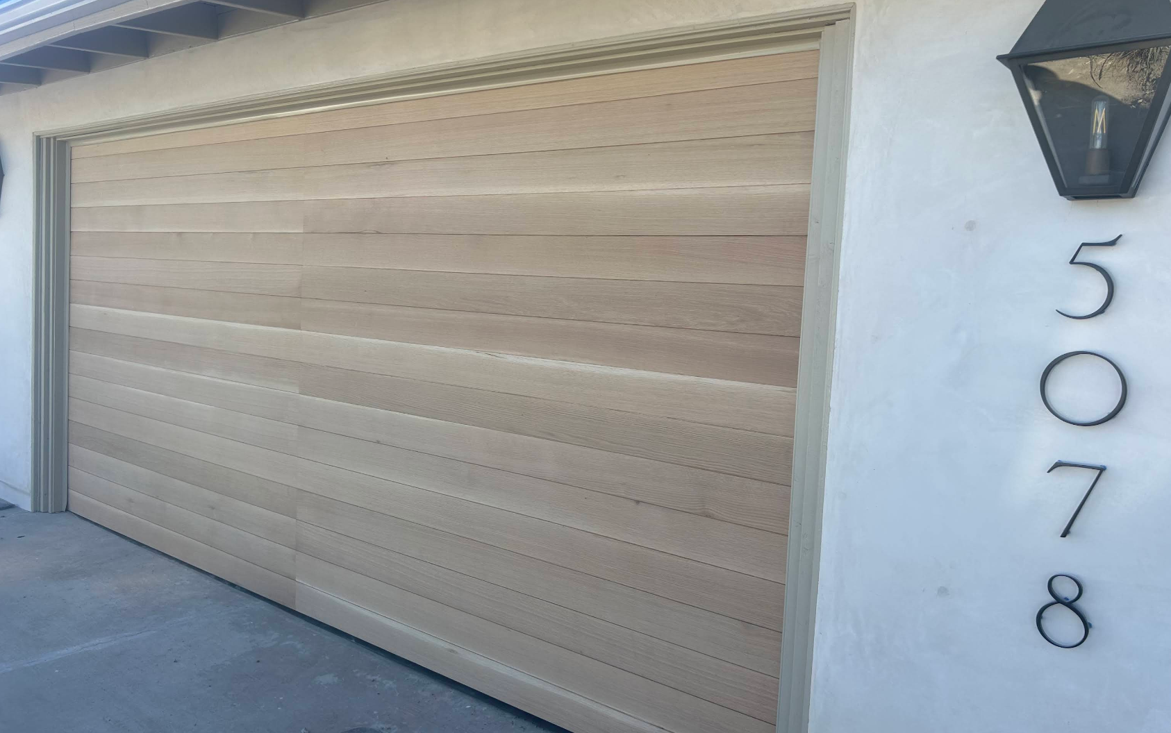 Beige garage door beside house number 5078 on a white exterior wall