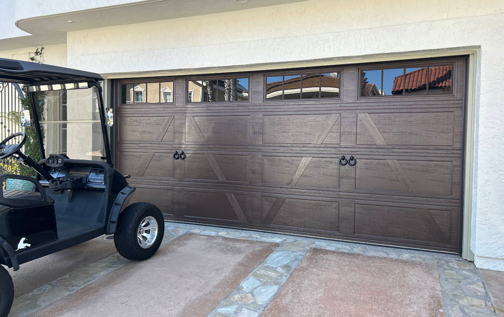 Brown garage doors beside a driveway, with part of a black utility cart visible on the left.