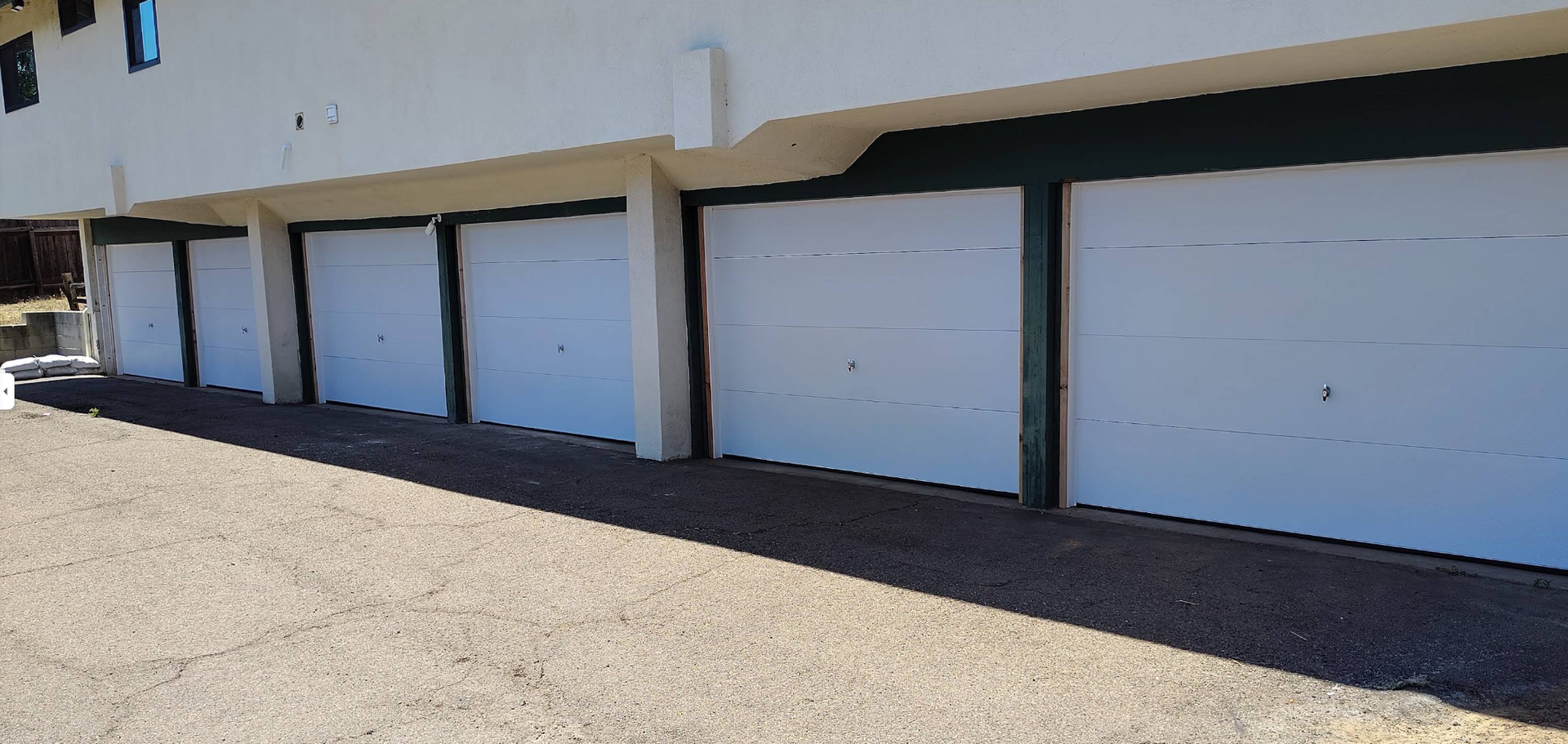 Row of white garage doors on a tan industrial building in bright sunlight