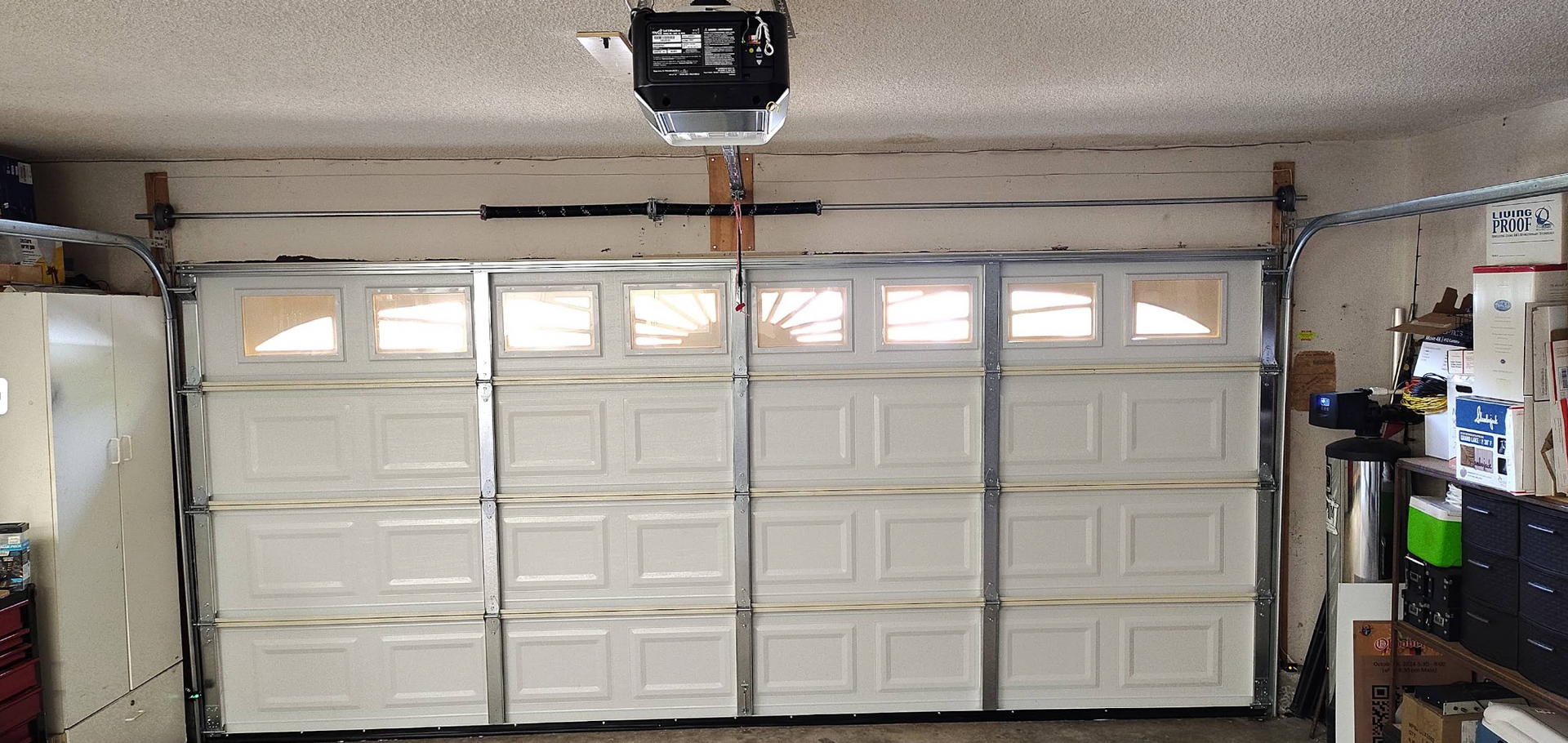 Garage interior with white paneled door and overhead opener, shelves on the right side