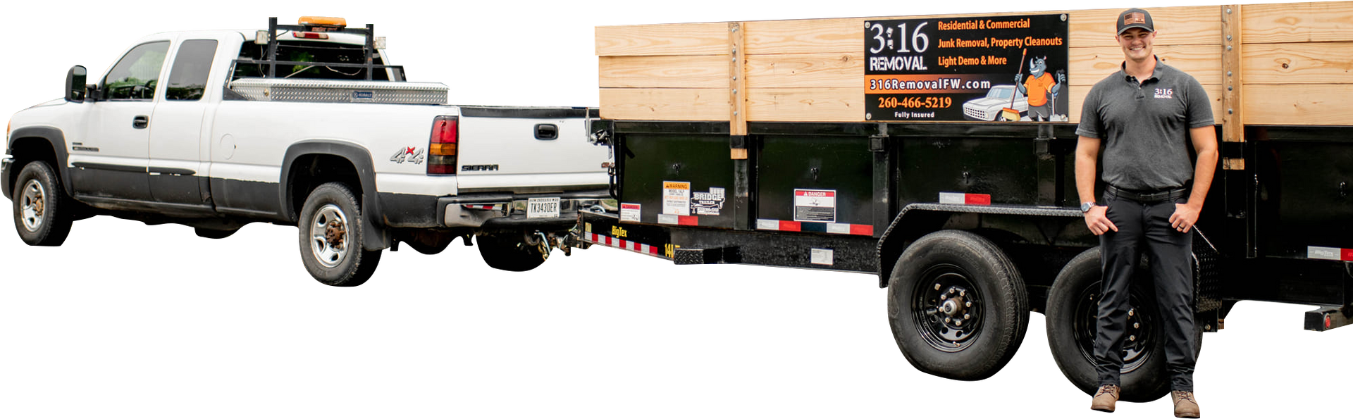A white truck pulling a black trailer loaded with wood. A man stands beside the trailer.