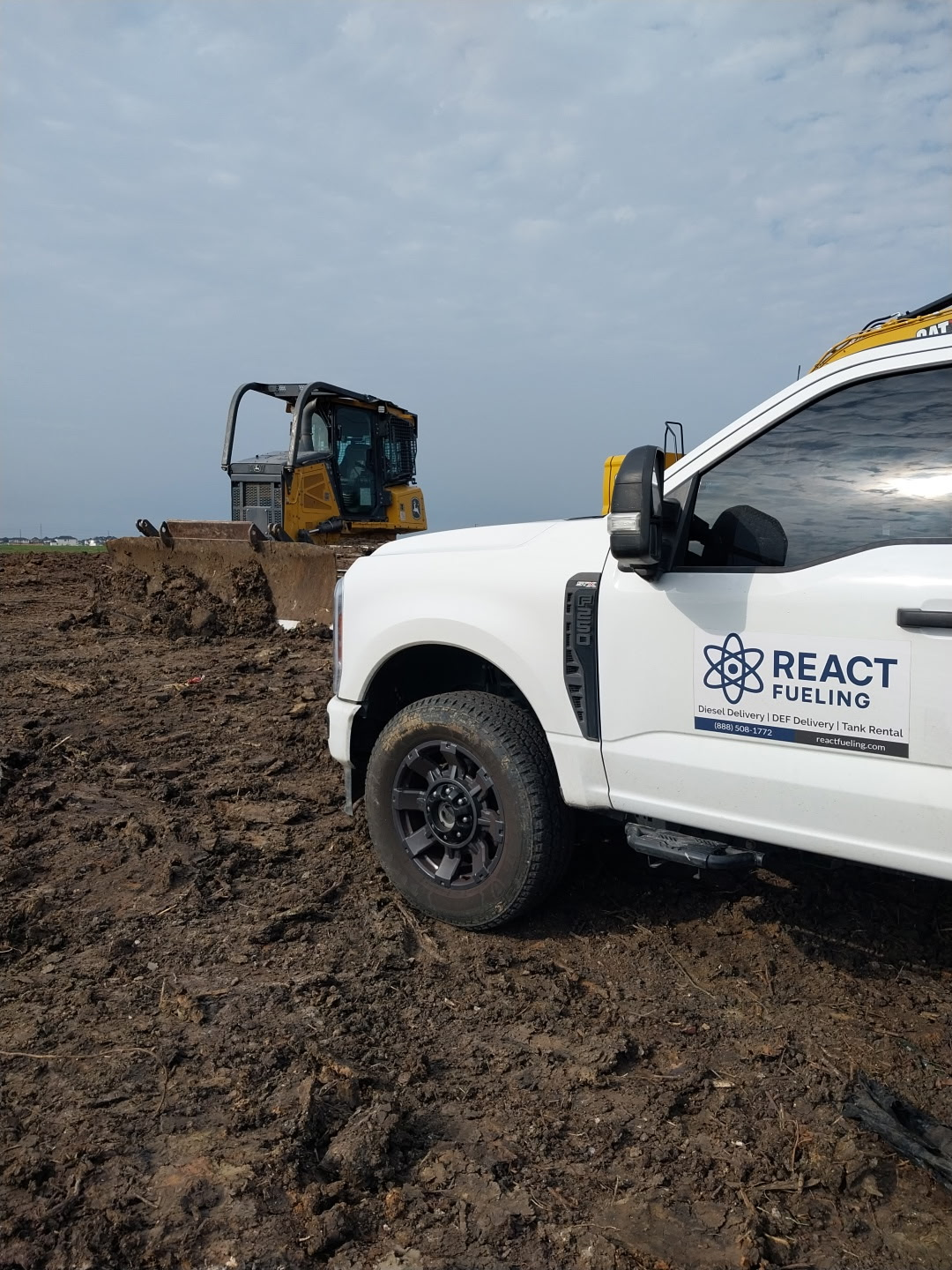 White REACT truck beside a muddy construction site with an excavator under a cloudy sky