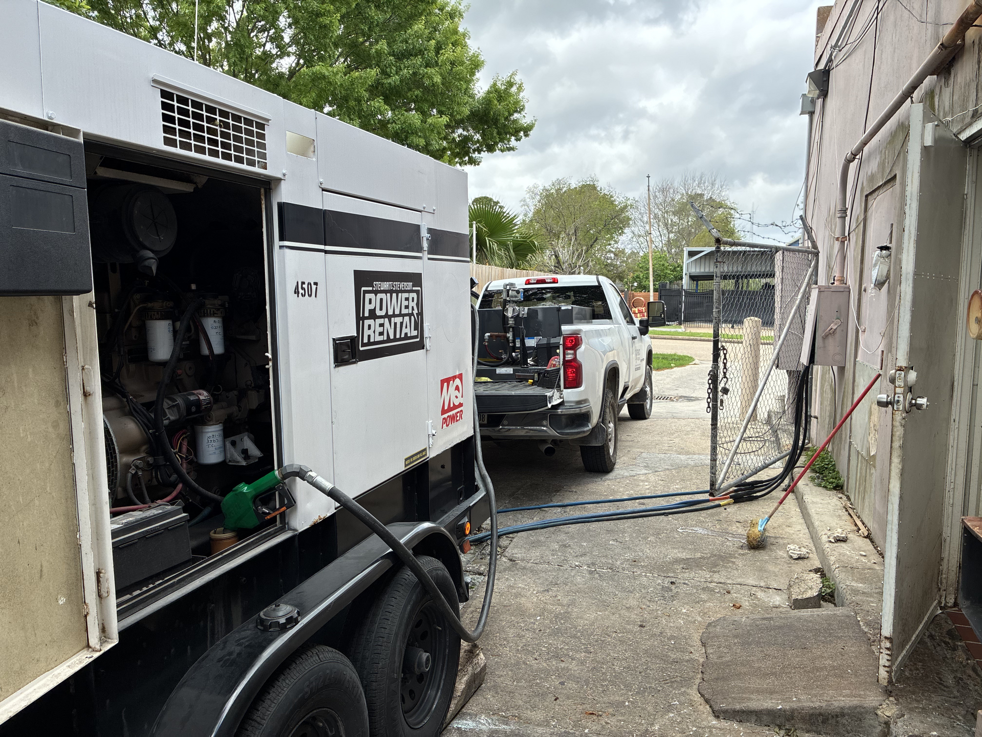 White utility truck with equipment parked in a narrow gravel alley beside a building.