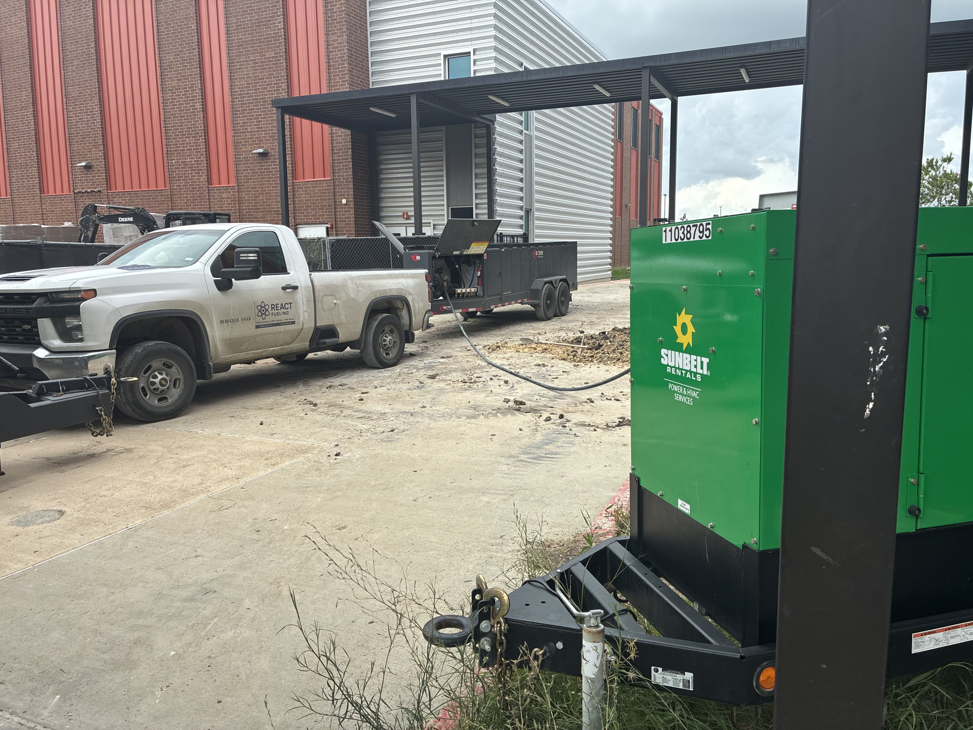 Green generator and pickup truck outside a brick building under a metal canopy