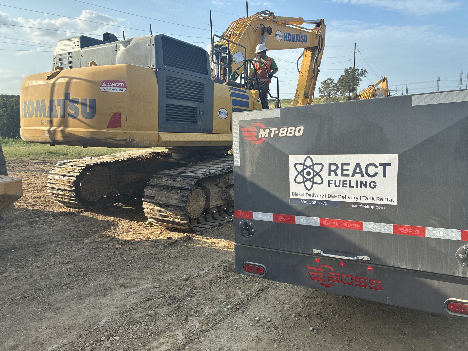 Yellow excavator beside a gray fuel truck labeled “React Fueling” at a construction site