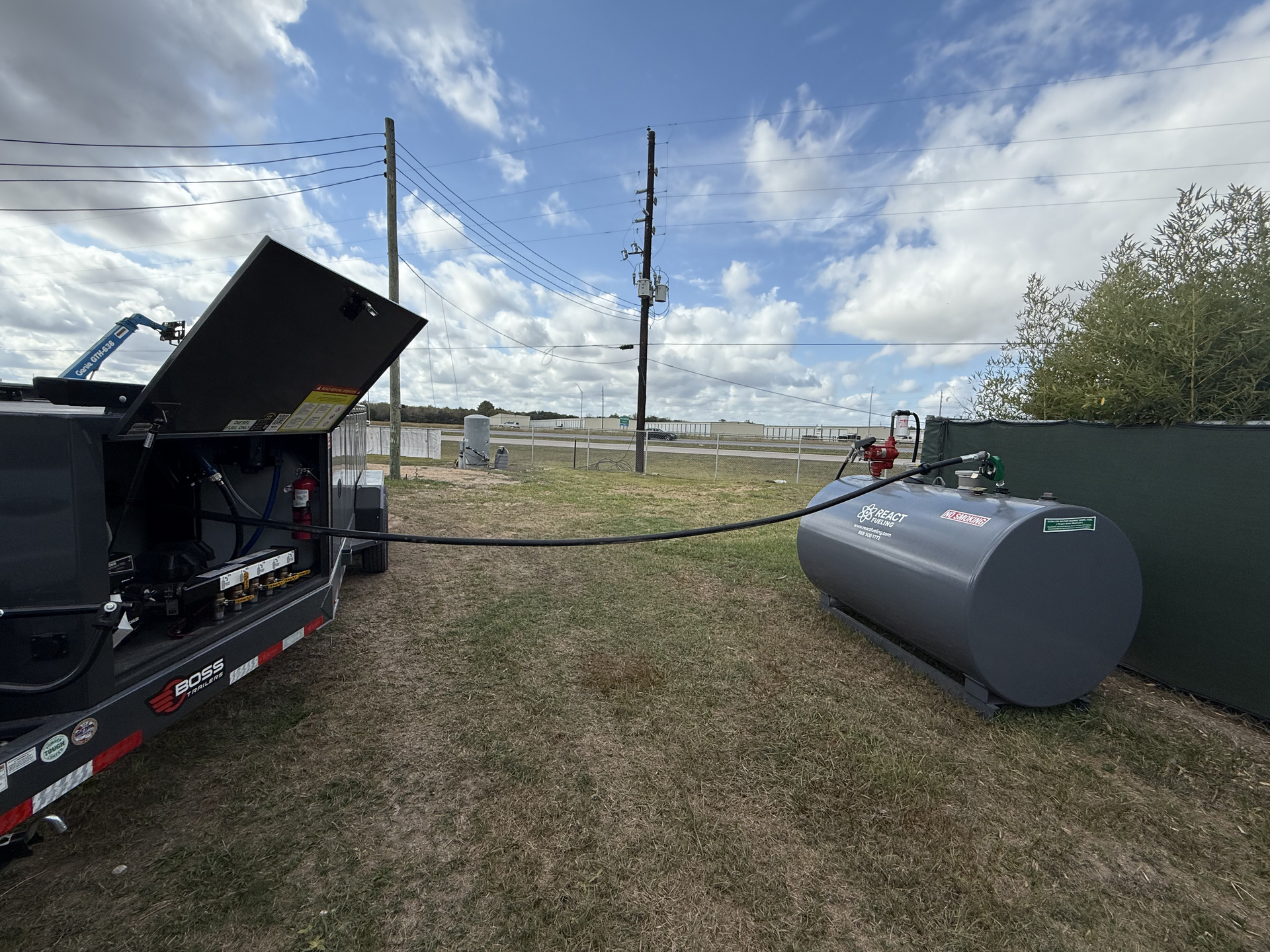 Industrial trailer with open hatch and a gray fuel tank on a grassy field under a cloudy sky