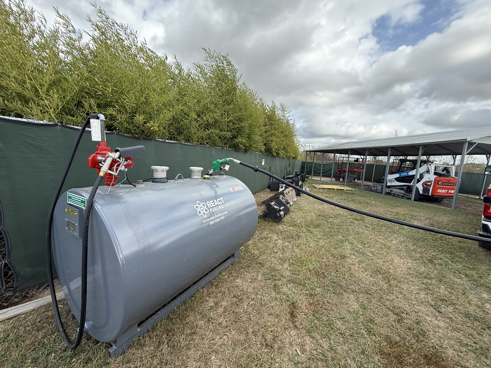 Gray fuel tank with red pumps in an outdoor yard under cloudy skies