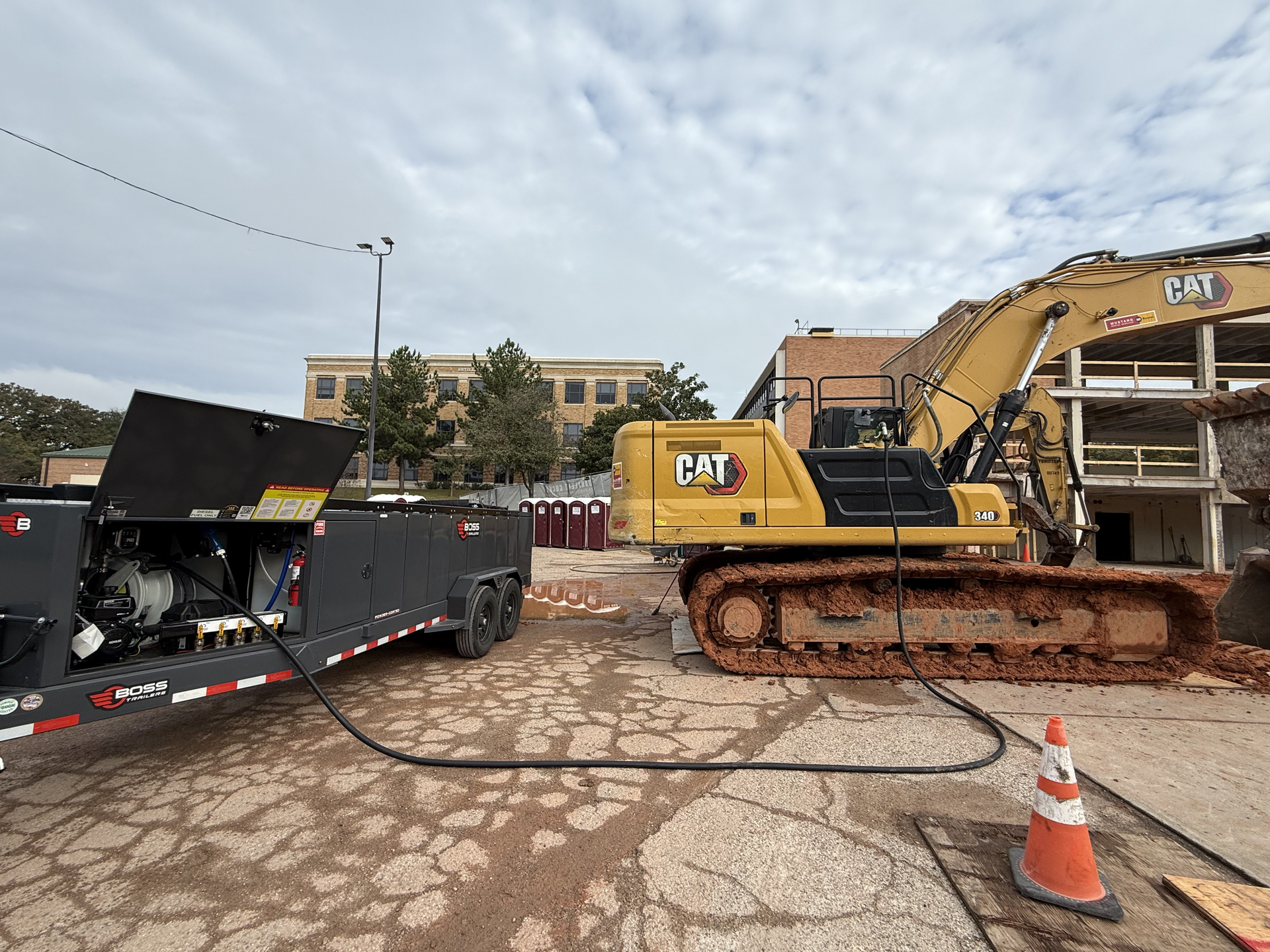 Excavator and dump trailer at a muddy construction site with an orange cone in front.