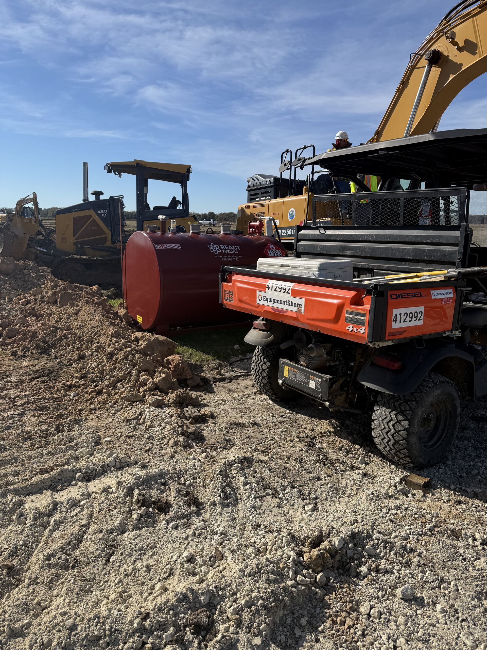 Construction equipment moving gravel beside a red tank and excavator in a quarry