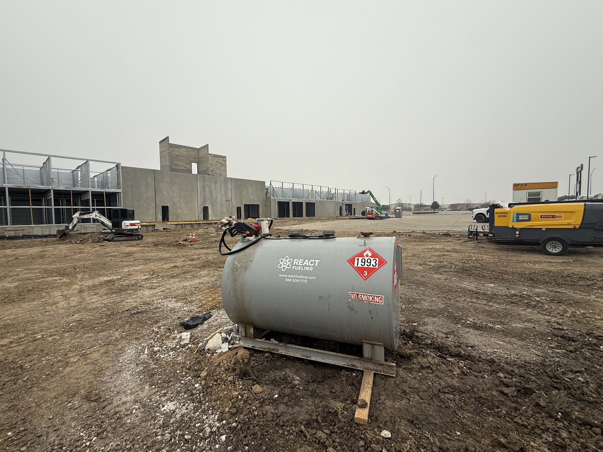 Construction site with a gray fuel tank in the foreground and equipment and buildings in the background
