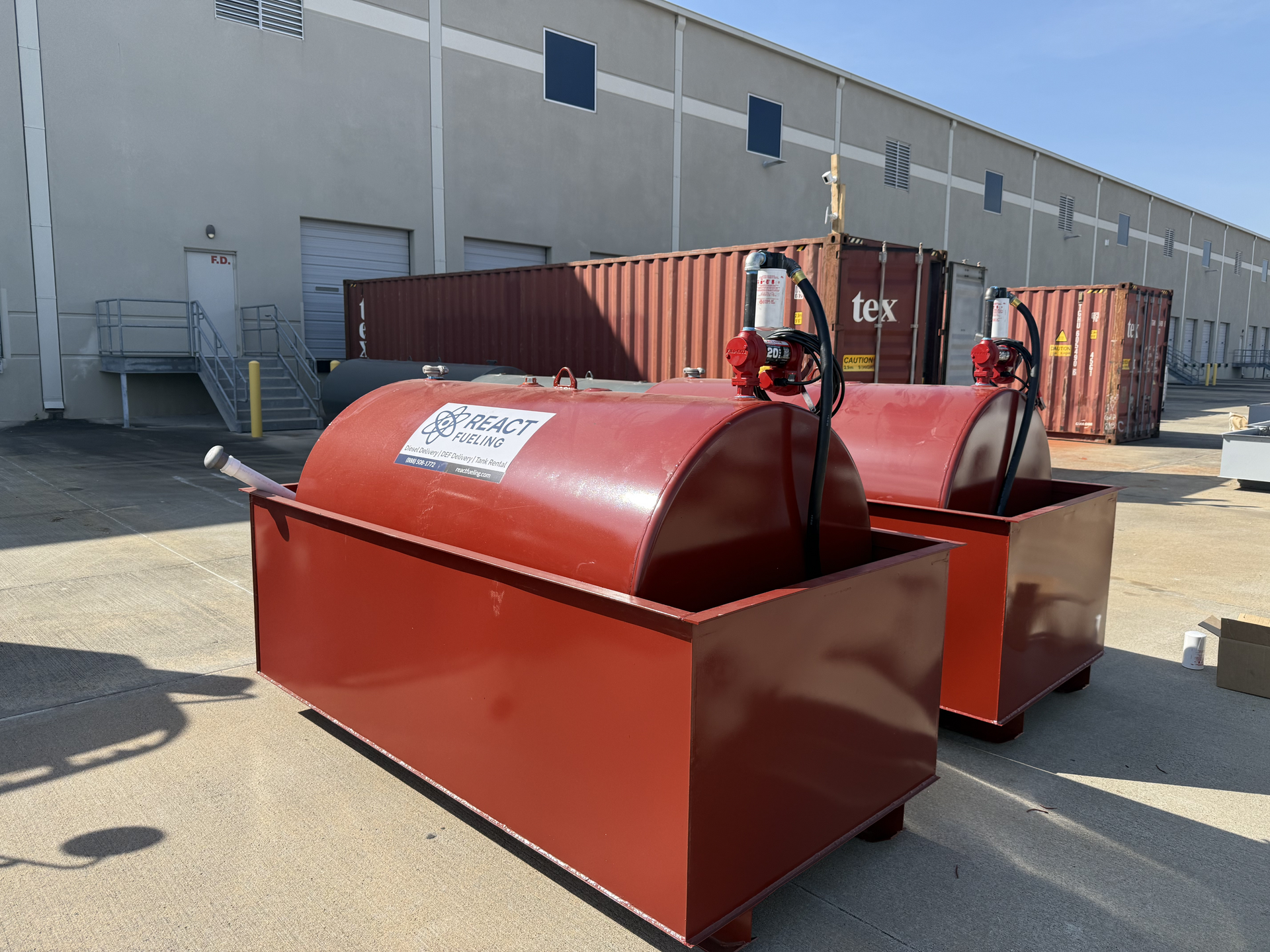 Two red industrial bins with hose reels parked outside a warehouse on a sunny day