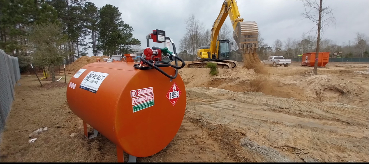 Orange tank in a muddy construction site with excavator and dirt piles in the background