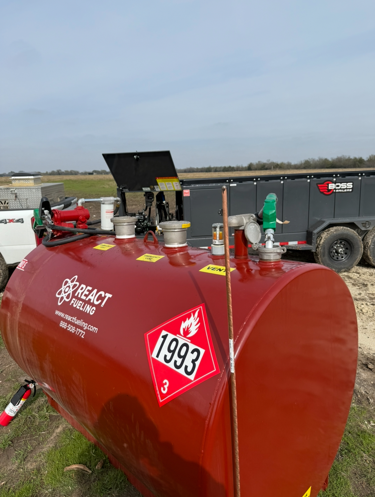 Red agricultural tanker trailer with equipment and a 1999 sign in a rural field.
