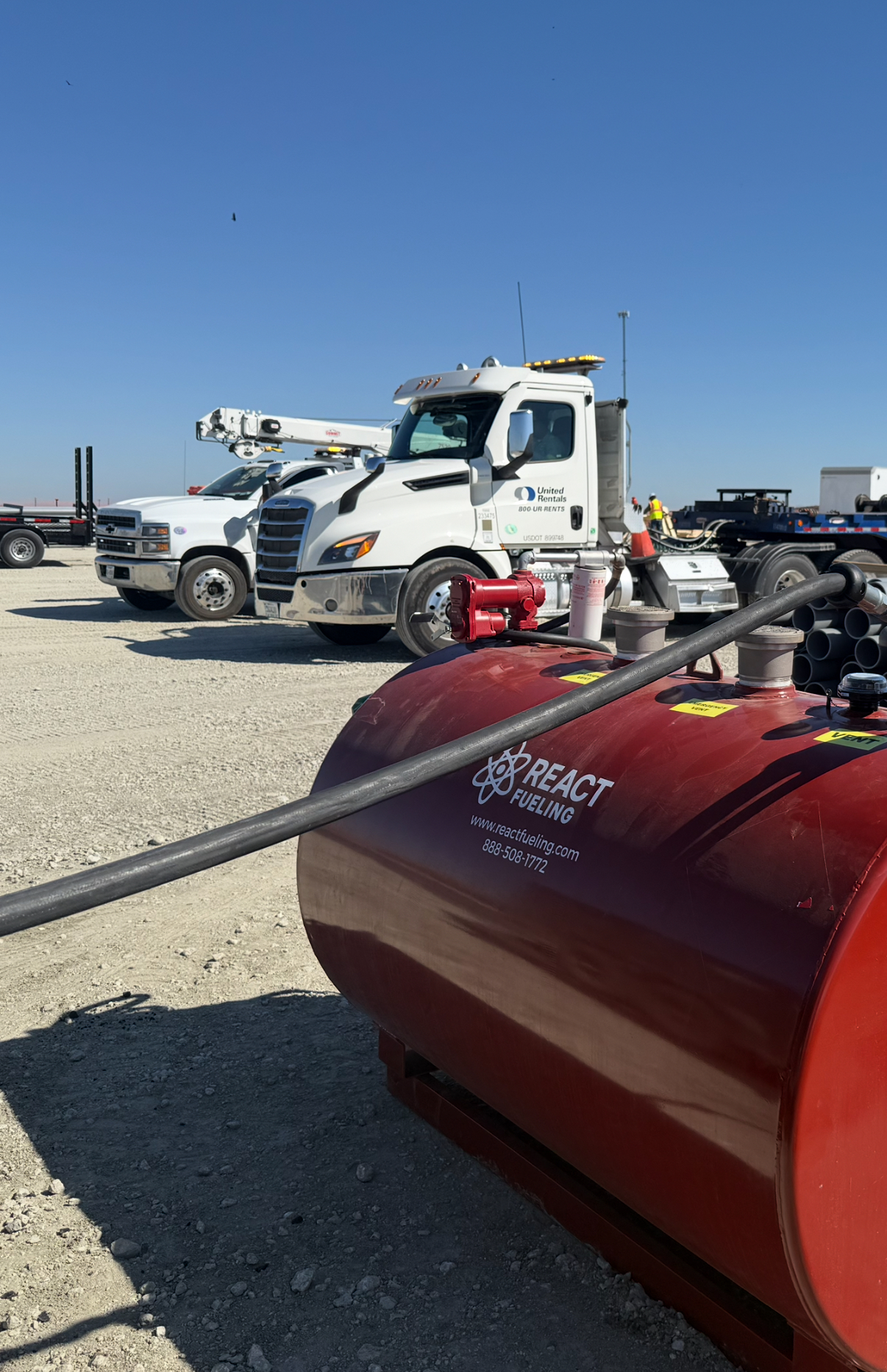 Red snowplow in foreground with white utility truck in a gravel lot under a clear blue sky
