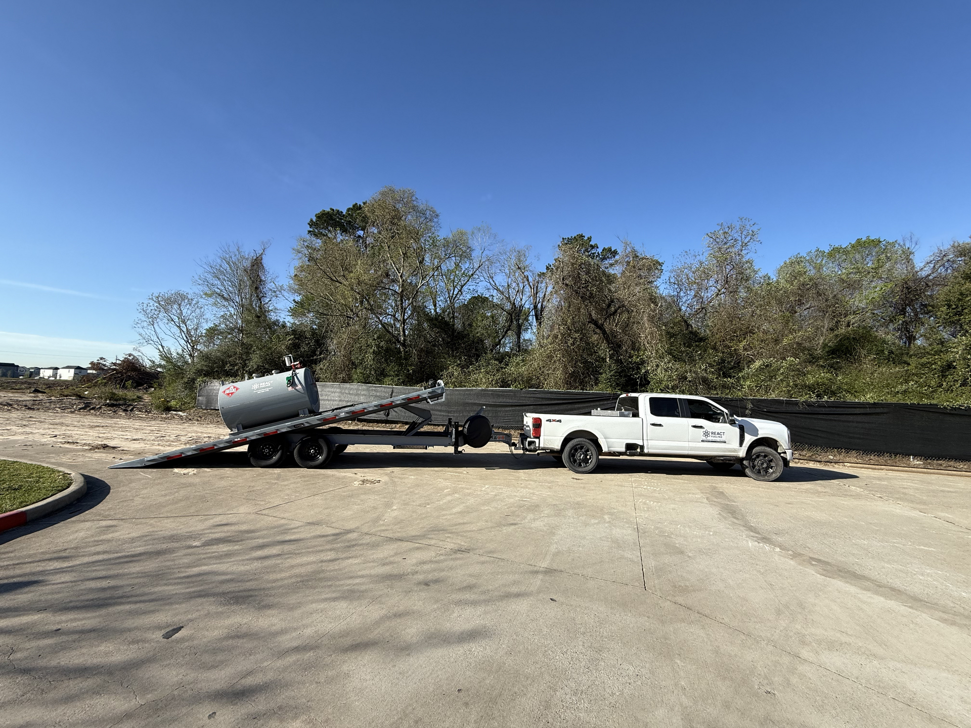 White pickup truck towing a trailer on a paved lot under a clear blue sky