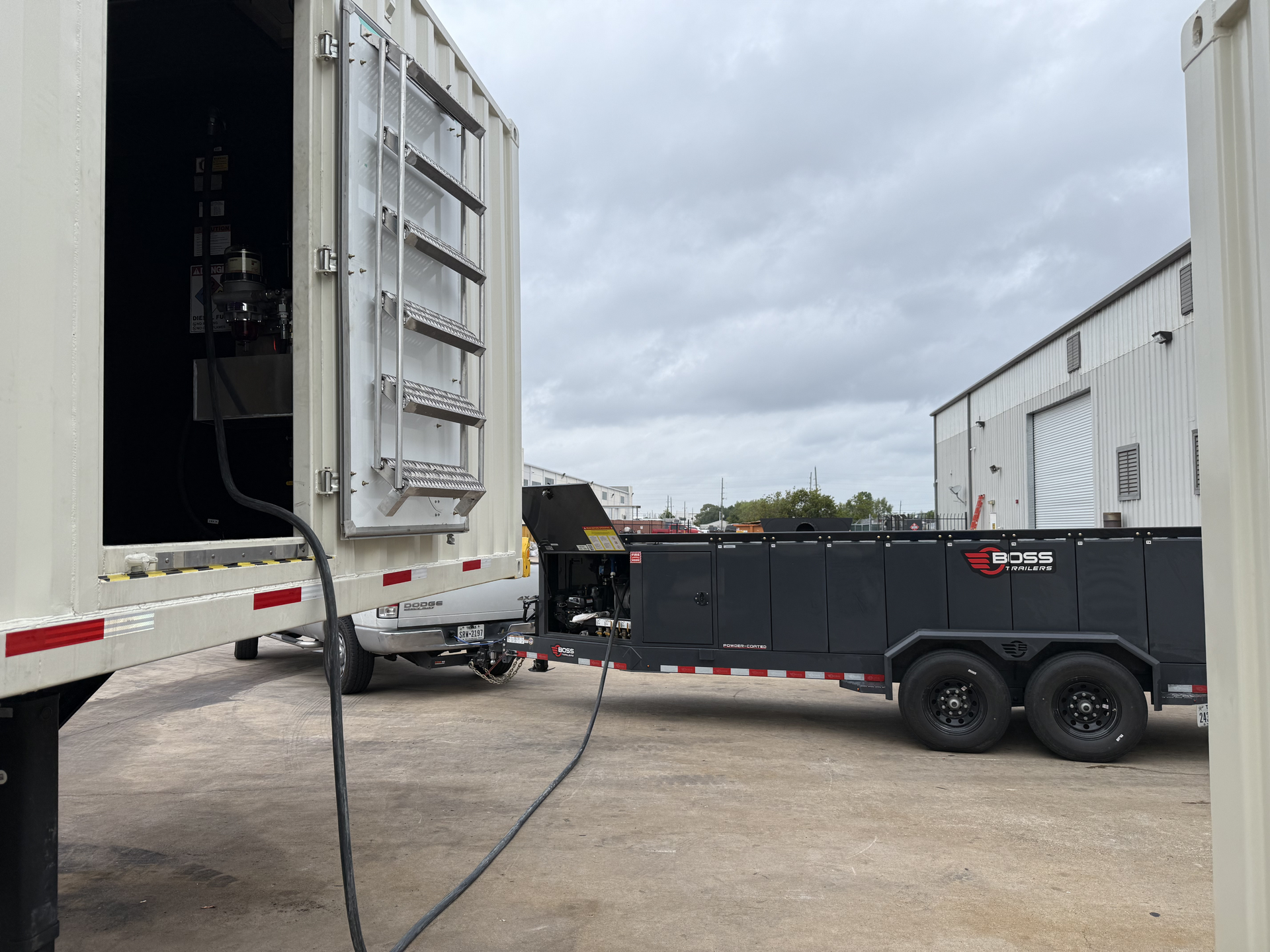 Industrial yard with open trailer doors and a black dump trailer parked between white trucks