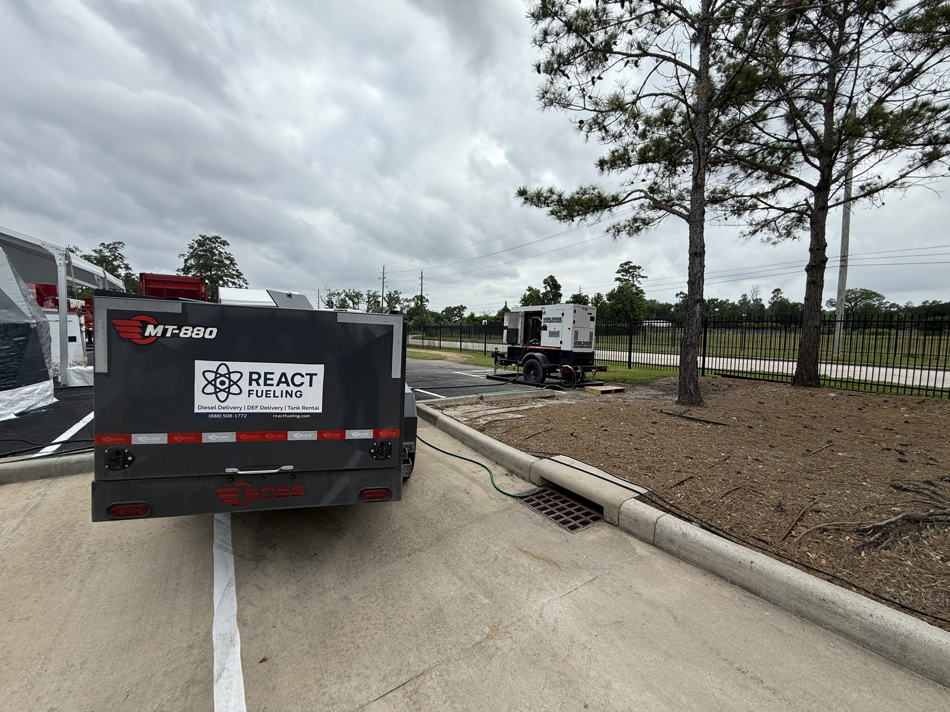 Black utility truck on a sandy roadside near a fenced area under cloudy sky