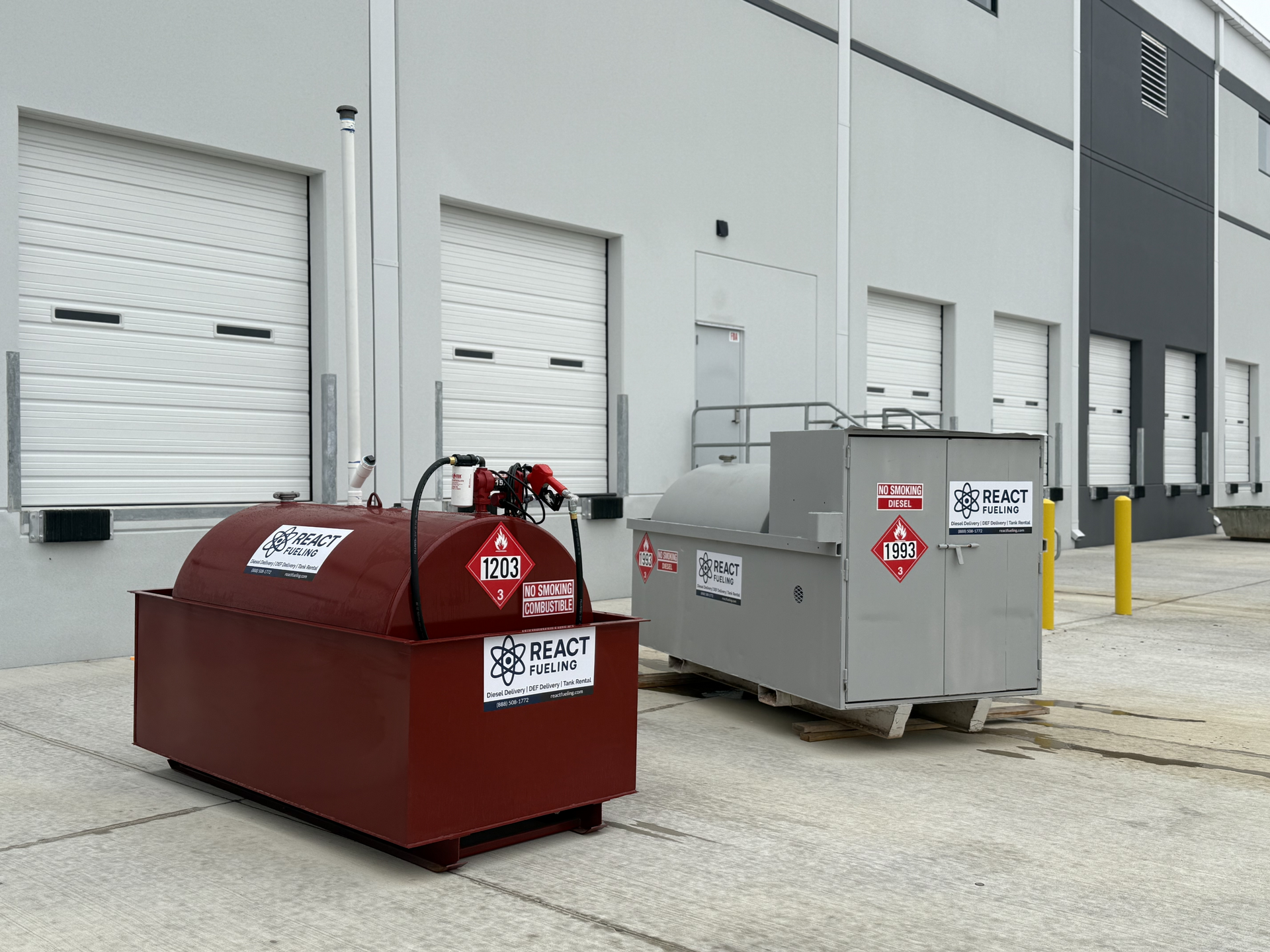 Two industrial waste bins, one red and one gray, outside a warehouse loading dock.