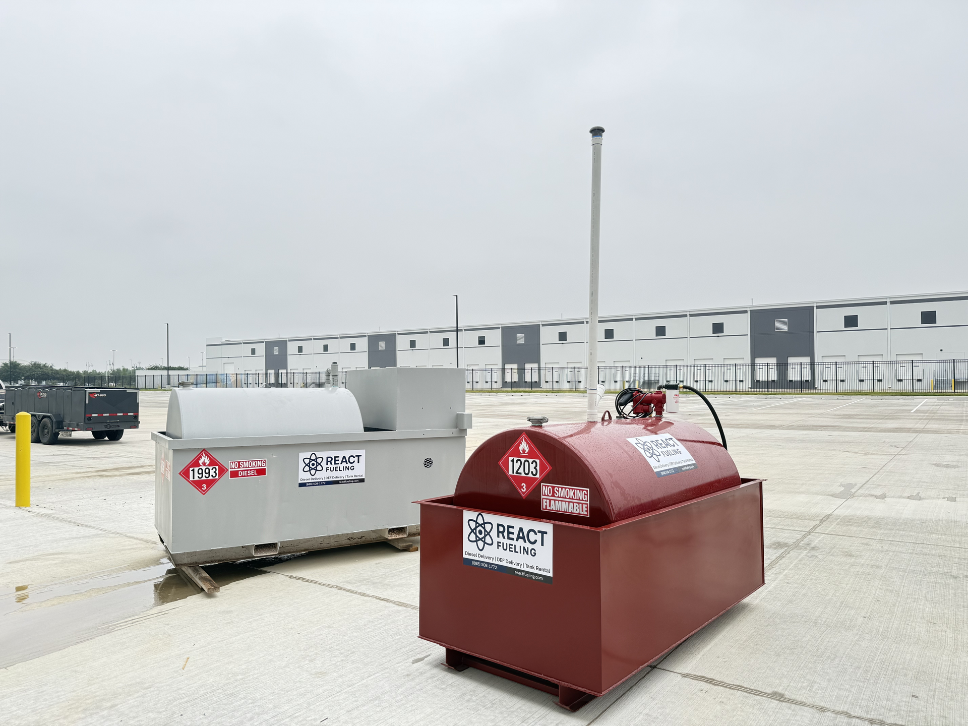 Two large outdoor industrial tanks, one red and one gray, in a parking lot near a warehouse building.