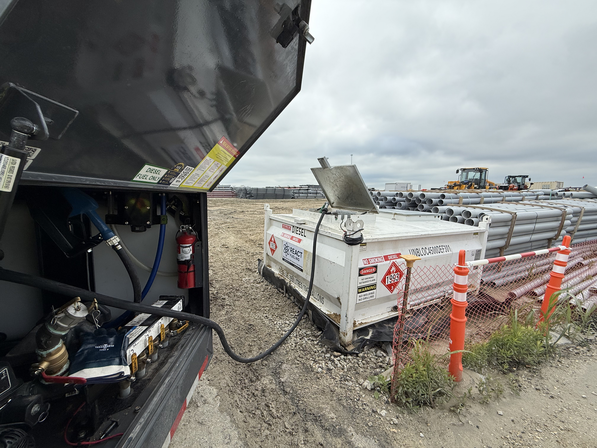Construction site with a dump truck, white equipment container, and orange safety posts on muddy ground