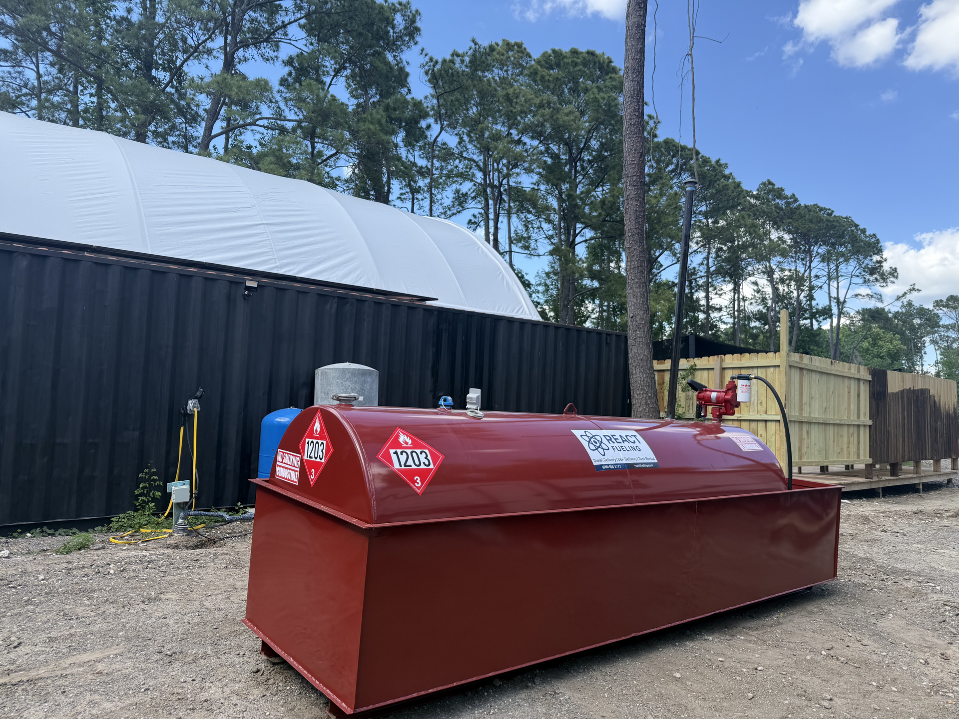 Red industrial equipment tank beside a black building and fence on a sunny day